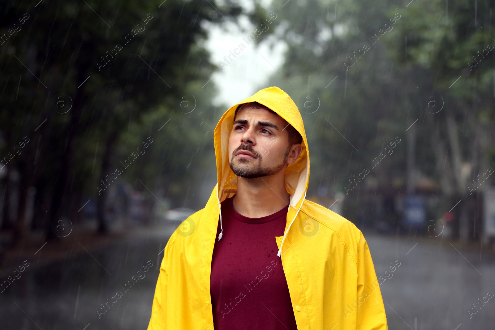 Photo of Thoughtful young man in bright coat outdoors on rainy day