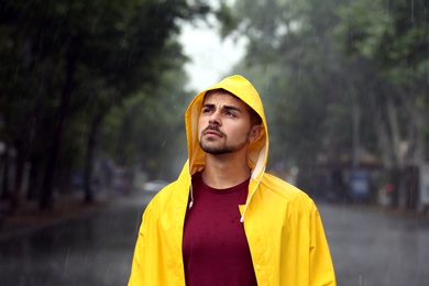 Thoughtful young man in bright coat outdoors on rainy day