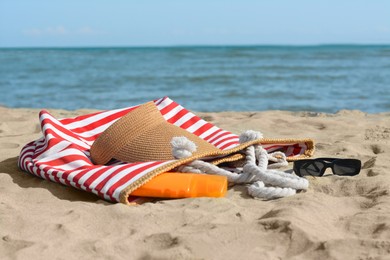 Photo of Stylish striped bag with beach accessories on sand near sea