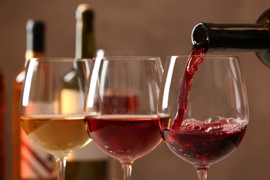 Pouring wine from bottle into glass on blurred background, closeup