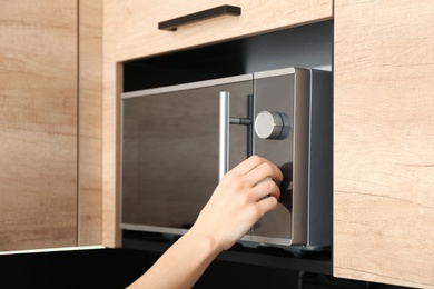 Photo of Young woman adjusting modern microwave oven in kitchen, closeup