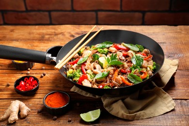 Stir-fry. Tasty noodles with meat in wok, chopsticks and ingredients on wooden table