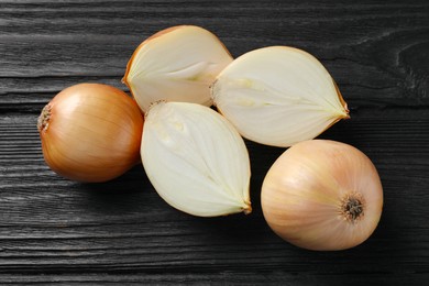 Photo of Whole and cut onions on black wooden table