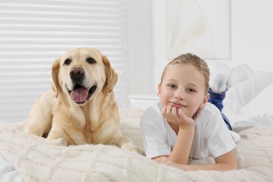 Photo of Cute child with her Labrador Retriever on bed at home. Adorable pet