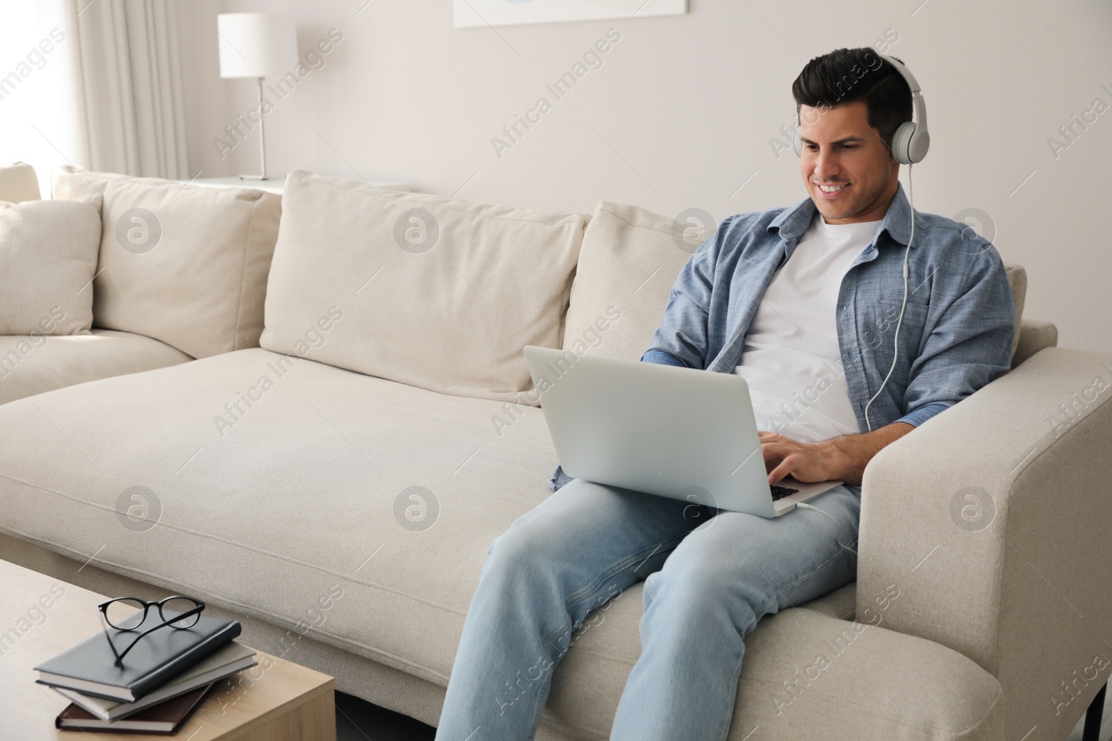 Photo of Man with laptop and headphones sitting on sofa at home