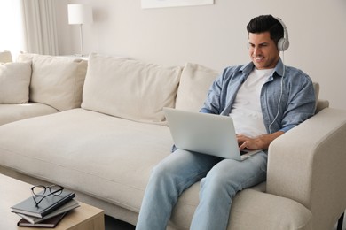 Man with laptop and headphones sitting on sofa at home