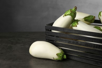 Photo of Wooden crate with white eggplants on black textured table against grey background. Space for text
