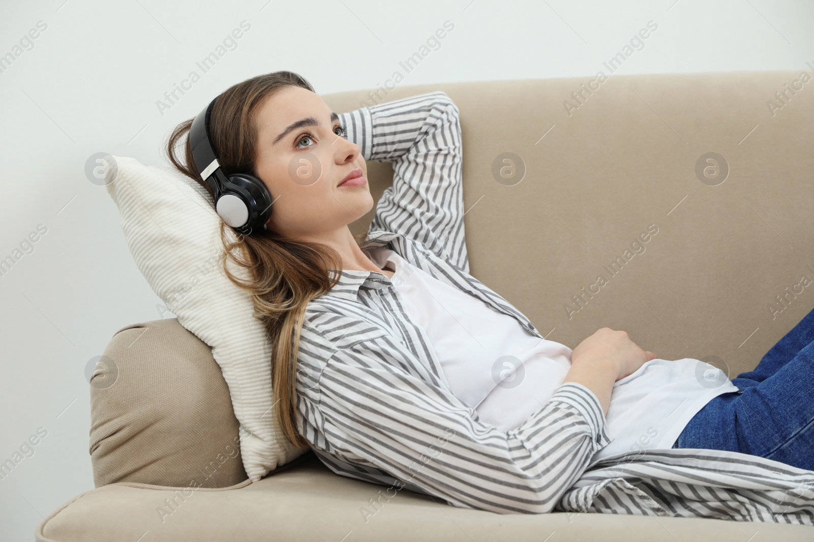 Photo of Young woman with headphones on sofa at home