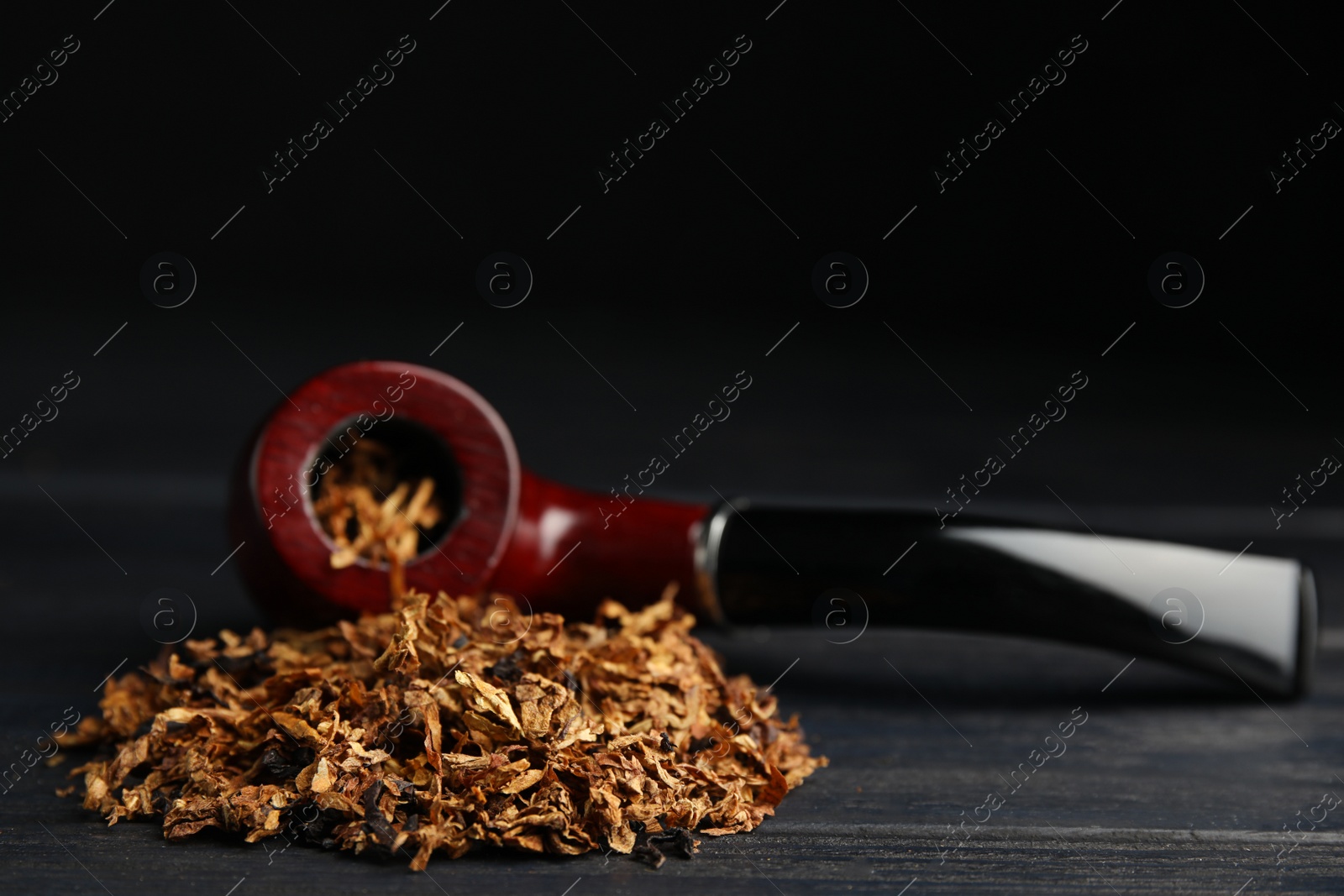 Photo of Smoking pipe and dry tobacco on black wooden table. Space for text