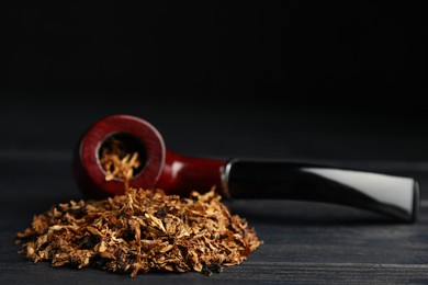 Smoking pipe and dry tobacco on black wooden table. Space for text