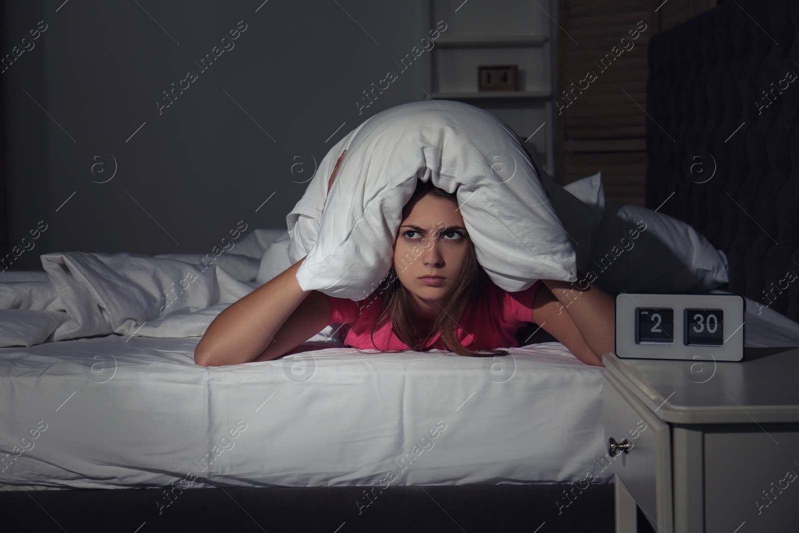 Photo of Young woman covering head with pillow in bed at home. Sleep disorder