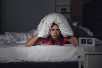 Photo of Young woman covering head with pillow in bed at home. Sleep disorder