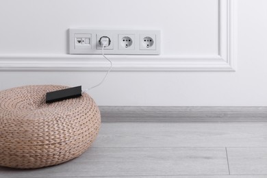 Photo of Power bank plugged into electric socket on white wall, space for text