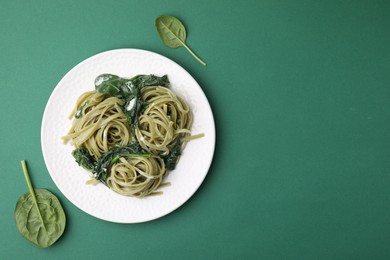 Photo of Tasty pasta with spinach and sauce on green table, flat lay. Space for text