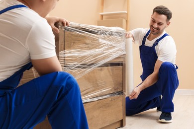 Workers wrapping chest of drawers in stretch film indoors