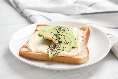 Slice of bread with spread and avocado on white wooden table