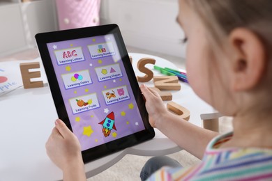 Photo of Little girl learning English with tablet indoors at online lesson, closeup