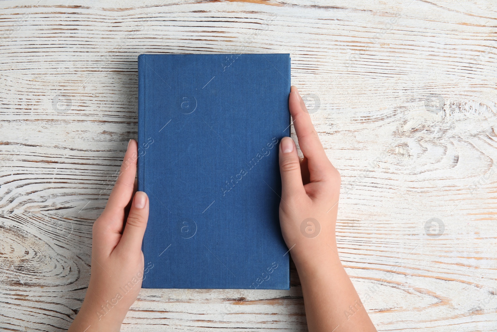 Photo of Woman holding hardcover book on white wooden background, top view