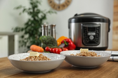 Photo of Two plates with delicious buckwheat and modern multi cooker on wooden table