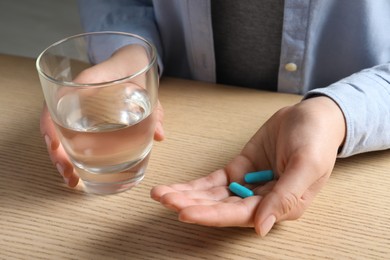 Woman with glass of water and pills at wooden table, closeup