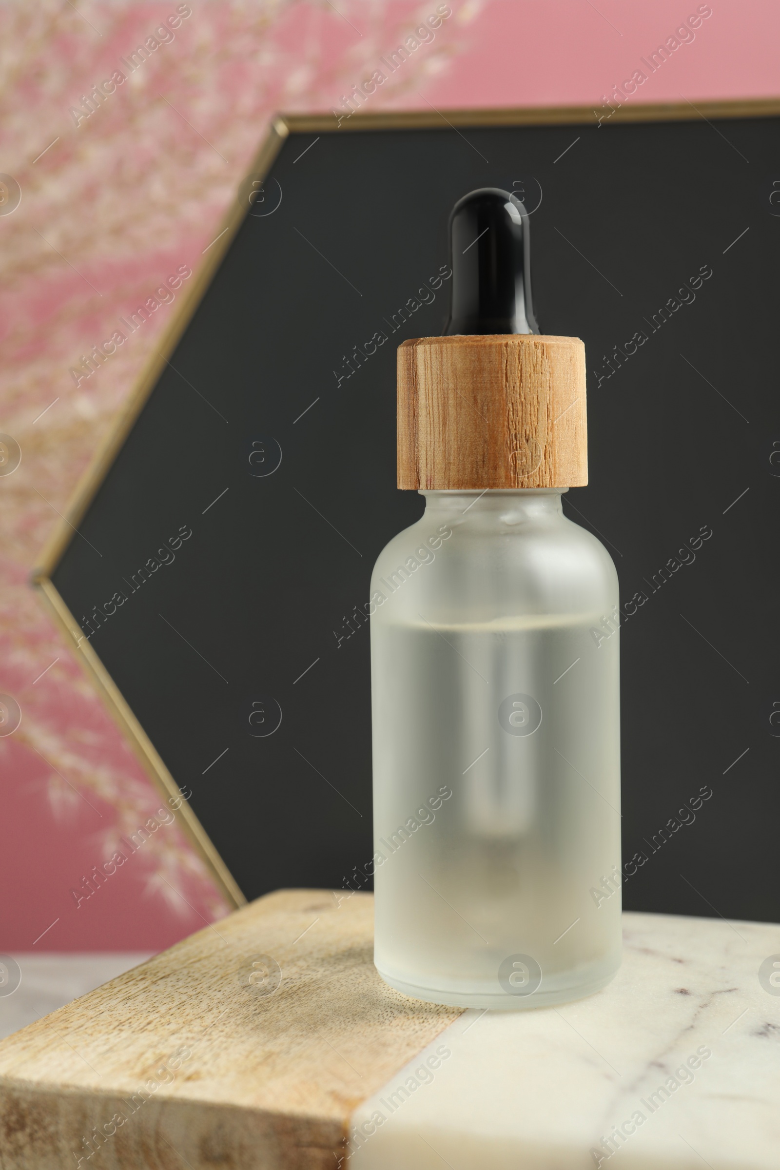 Photo of Bottle of face serum on marble board against pink background
