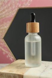 Bottle of face serum on marble board against pink background