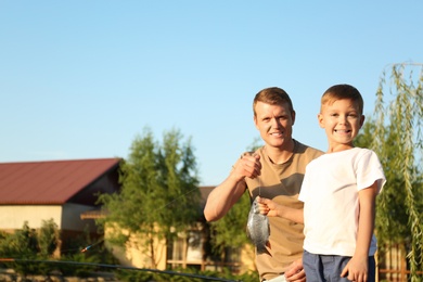 Photo of Dad and son fishing together on sunny day. Space for text