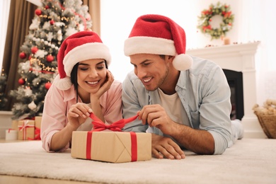 Photo of Happy couple in Santa hats with Christmas gift at home