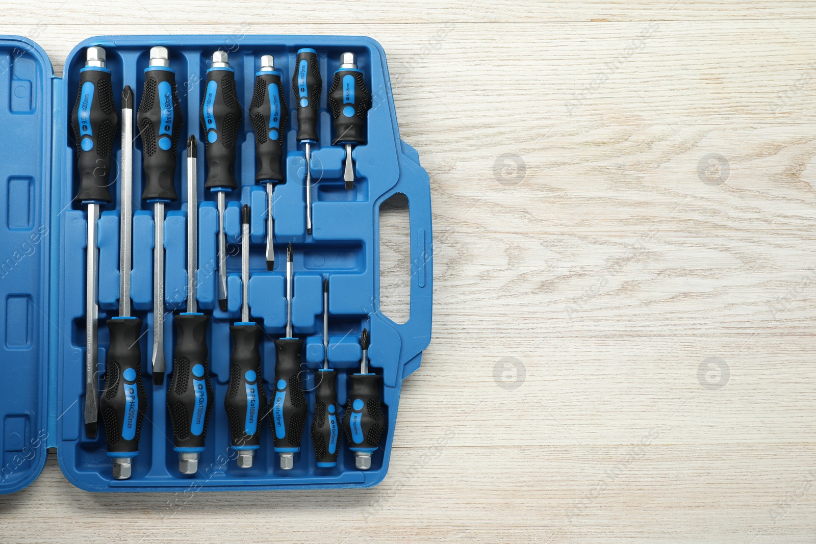 Photo of Set of screwdrivers in open toolbox on light wooden table, top view. Space for text