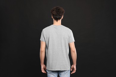 Photo of Man wearing light gray t-shirt on black background, back view. Mockup for design