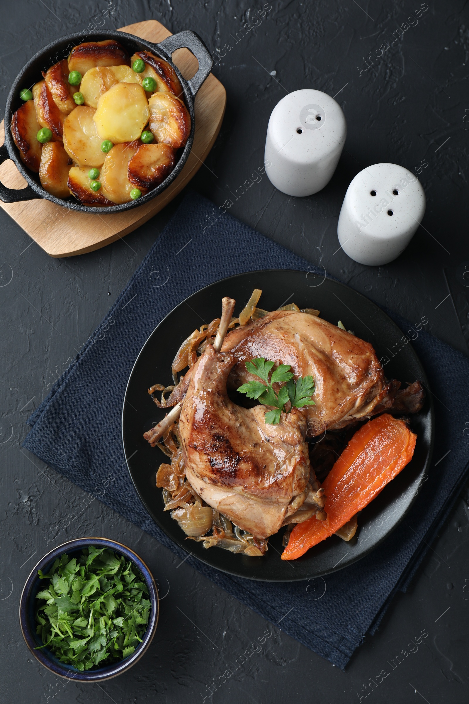 Photo of Tasty cooked rabbit meat with vegetables and potato served on black table, flat lay