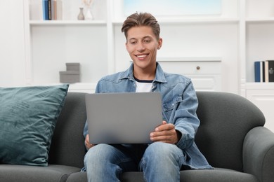 Happy young man having video chat via laptop on sofa indoors