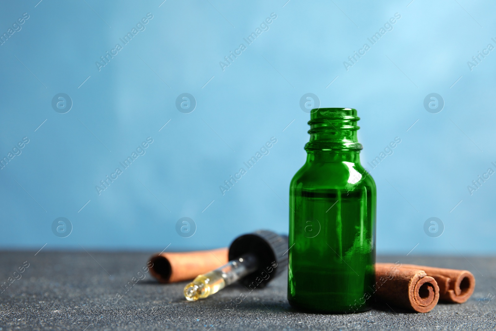 Photo of Bottle of essential oil and cinnamon sticks on table against blue background. Space for text