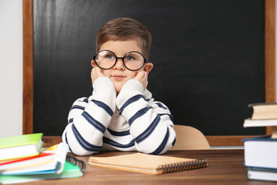 Cute little child wearing glasses at desk in classroom. First time at school