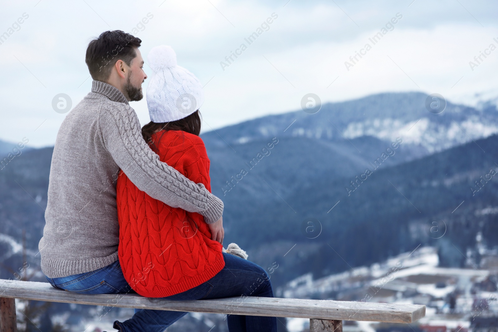 Photo of Couple sitting on bench and enjoying mountain landscape, space for text. Winter vacation