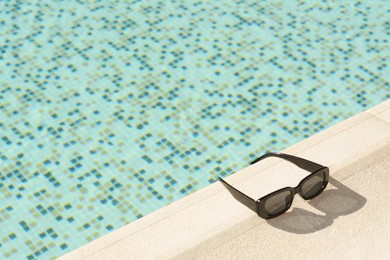 Photo of Stylish sunglasses near outdoor swimming pool on sunny day, space for text