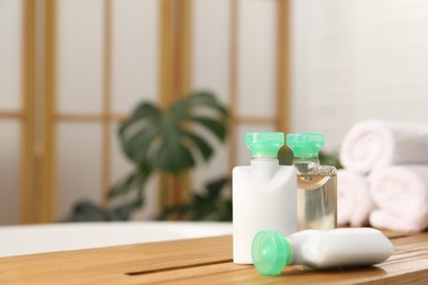 Photo of Wooden tray with mini bottles of cosmetic products on bath tub in bathroom. Space for text