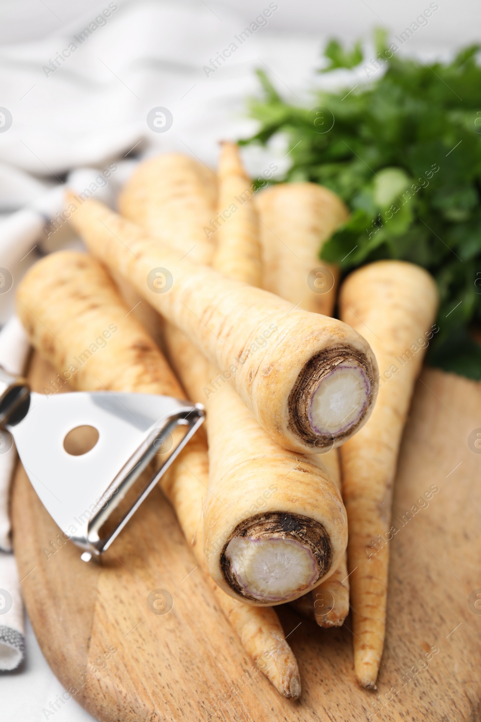 Photo of Raw parsley roots and peeler on table, closeup