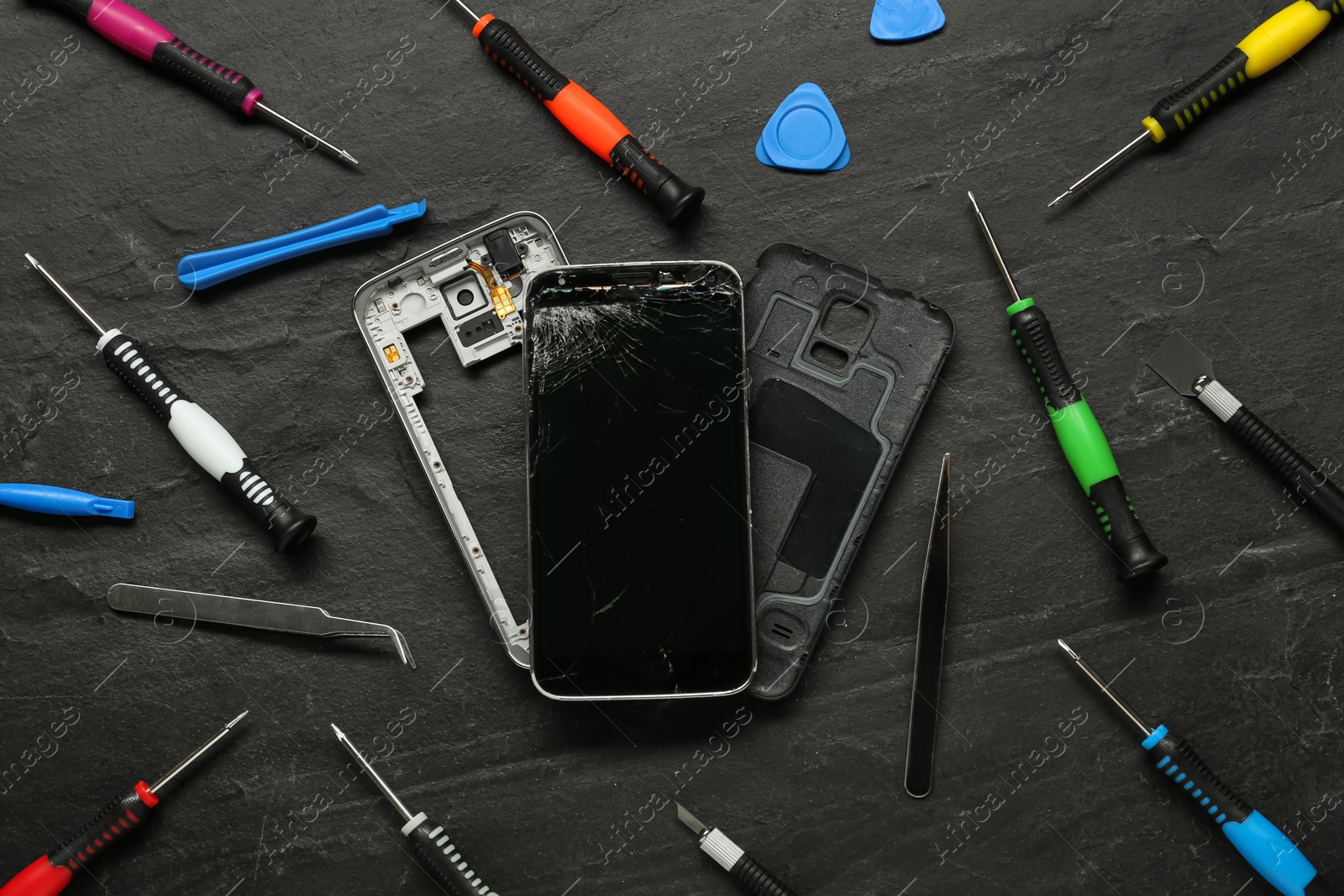 Photo of Damaged smartphone and repair tools on black background, flat lay