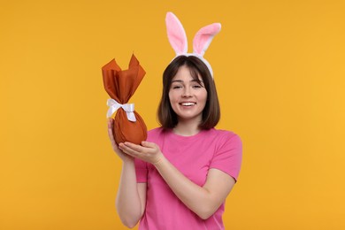 Photo of Easter celebration. Happy woman with bunny ears and wrapped egg on orange background