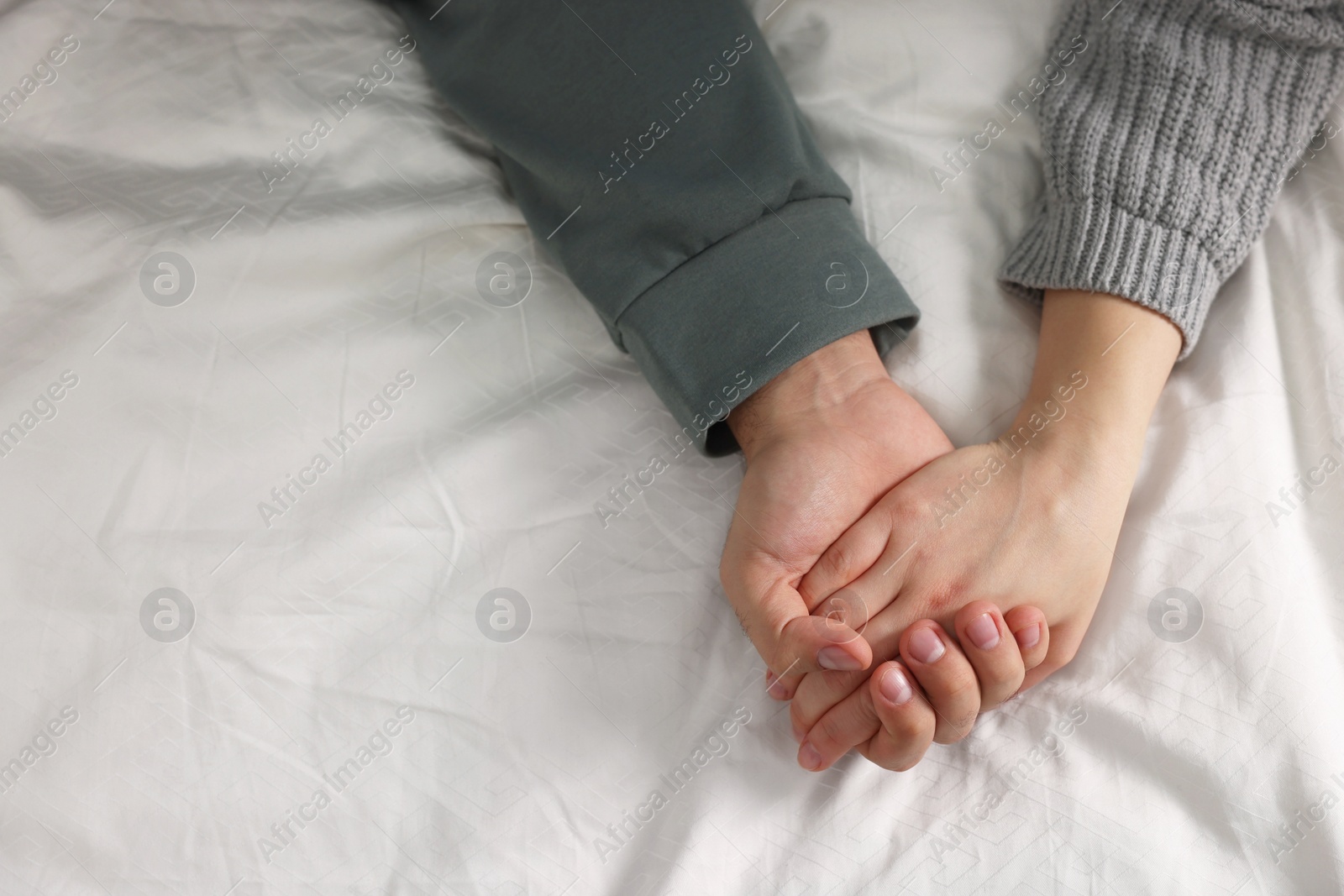 Photo of Couple holding hands on bed, above view. Space for text