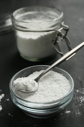 Baking powder in bowl, jar and spoon on black textured table, closeup