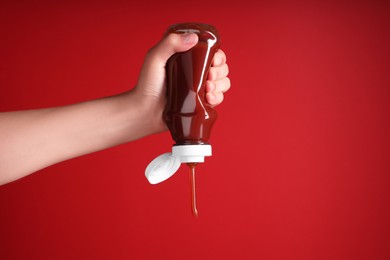 Photo of Woman pouring tasty ketchup from bottle on red background, closeup