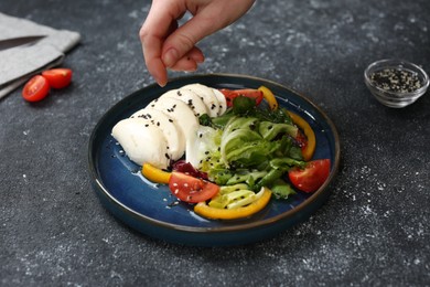 Food stylist preparing delicious salad with mozzarella and tomatoes for photoshoot at dark grey table in studio, closeup