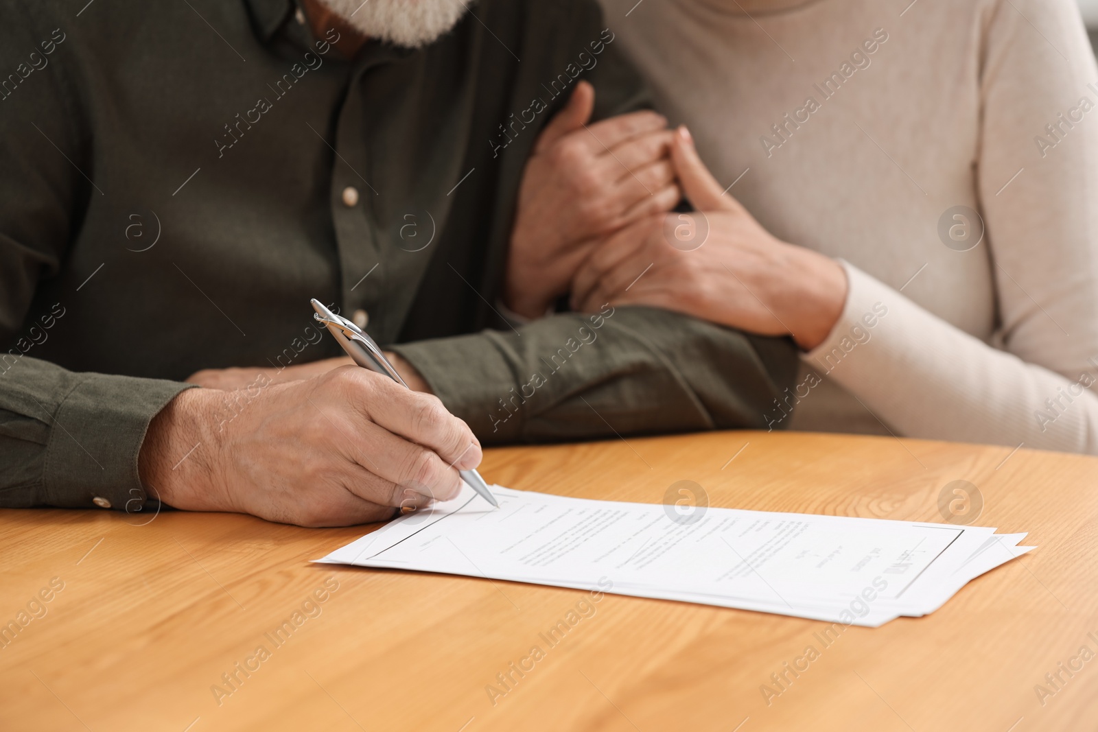 Photo of Senior couple signing Last Will and Testament at wooden table, closeup