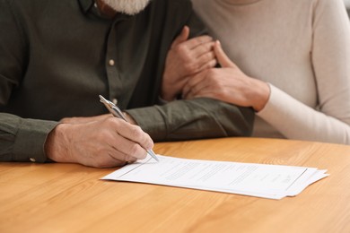 Senior couple signing Last Will and Testament at wooden table, closeup