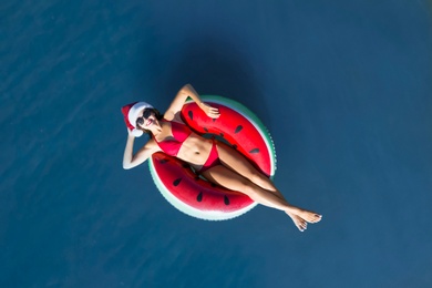 Young woman wearing Santa hat and bikini with inflatable ring in sea, top view. Christmas vacation