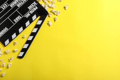Photo of Clapper board and popcorn on yellow background, flat lay with space for text. Visiting cinema