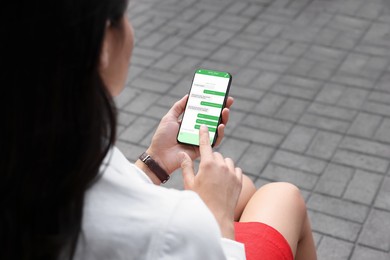 Woman texting via mobile phone outdoors, closeup. Device screen with messages