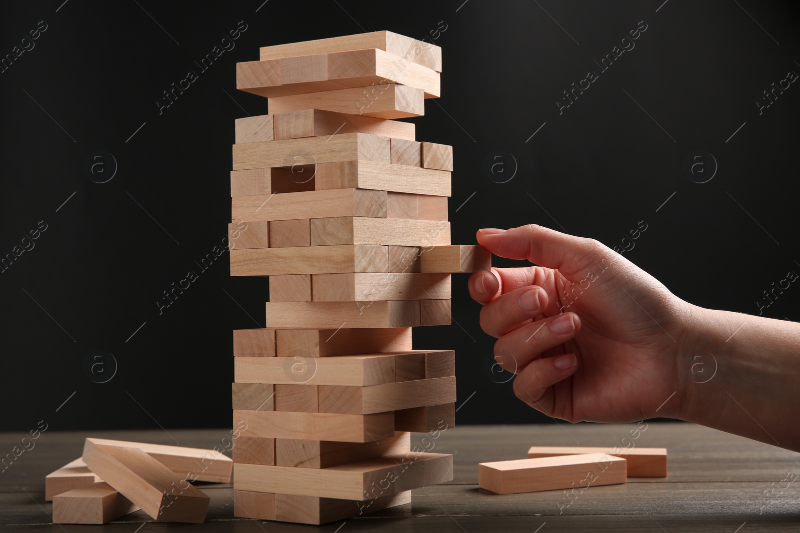 Photo of Woman playing Jenga at table against dark gray background, closeup